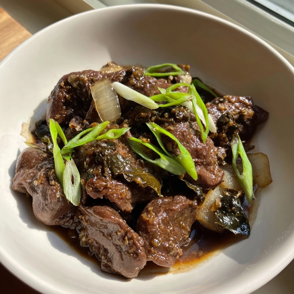 Close-up of Filipino Adobong Atay ng Manok, glistening with sauce, garnished with fresh scallions.