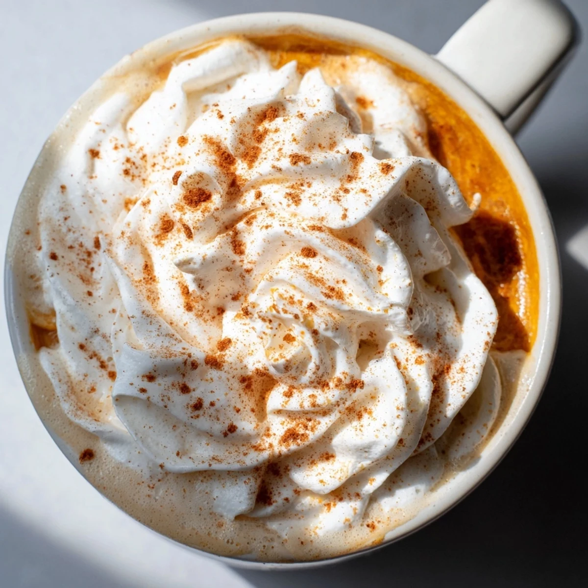 Steaming mug of Pumpkin Spice Latte, topped with whipped cream and cinnamon, ready to enjoy.