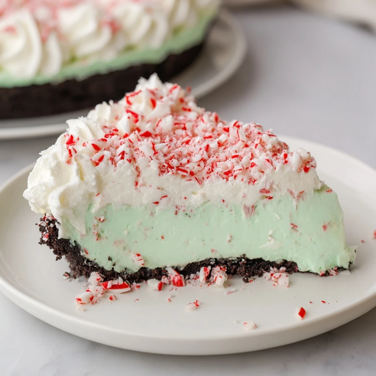 A slice of Peppermint Cheesecake, swirled with pink and topped with crushed peppermint candies.