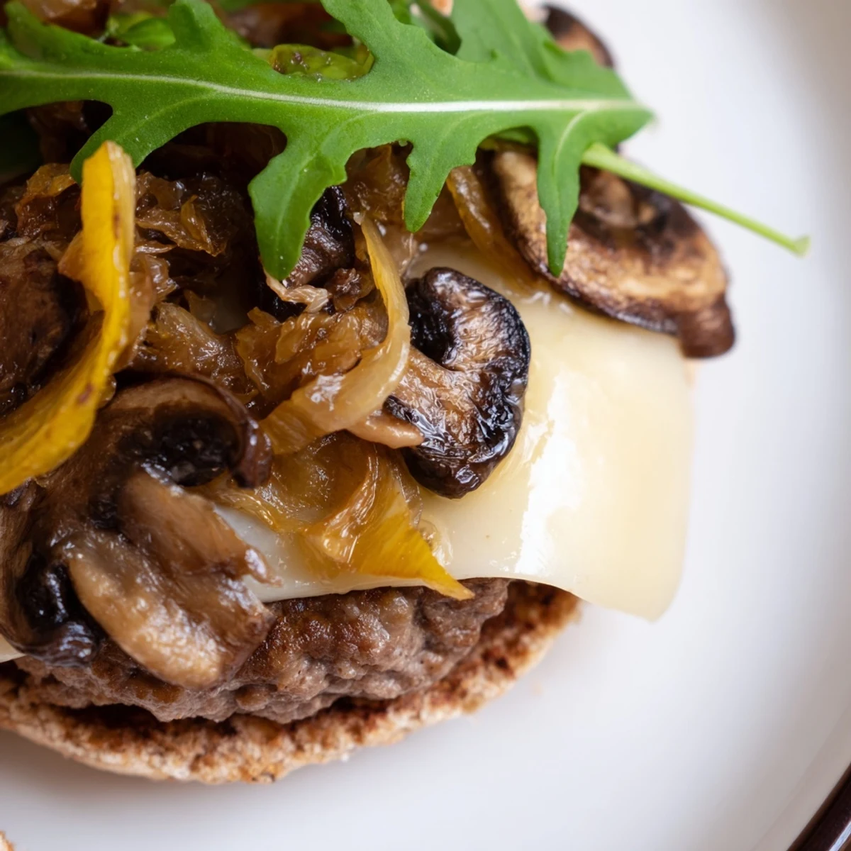Close-up of a Mushroom and Swiss Burger with seared beef, Swiss cheese, sautéed mushrooms, and caramelized onions resting on a white plate.