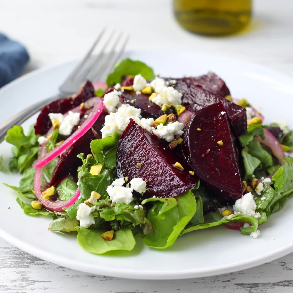 A plated serving of roasted beet salad with goat cheese and pistachios, drizzled with balsamic dressing for a vibrant side dish.