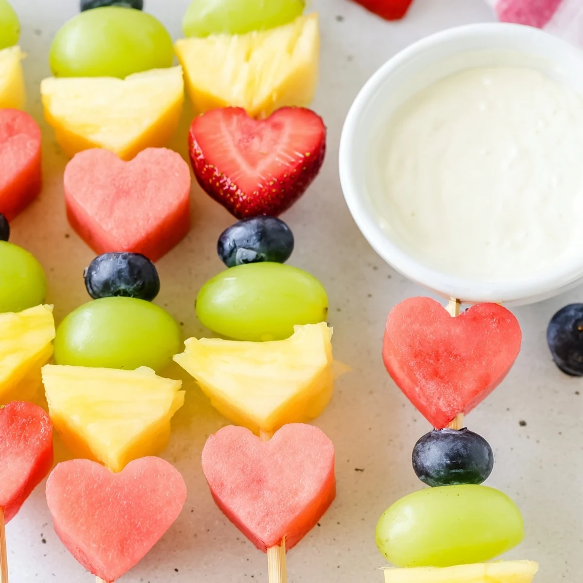 Colorful Sweetheart Fruit Skewers featuring juicy melon hearts and blueberries, served with a dollop of vanilla Greek yogurt dip for dipping.