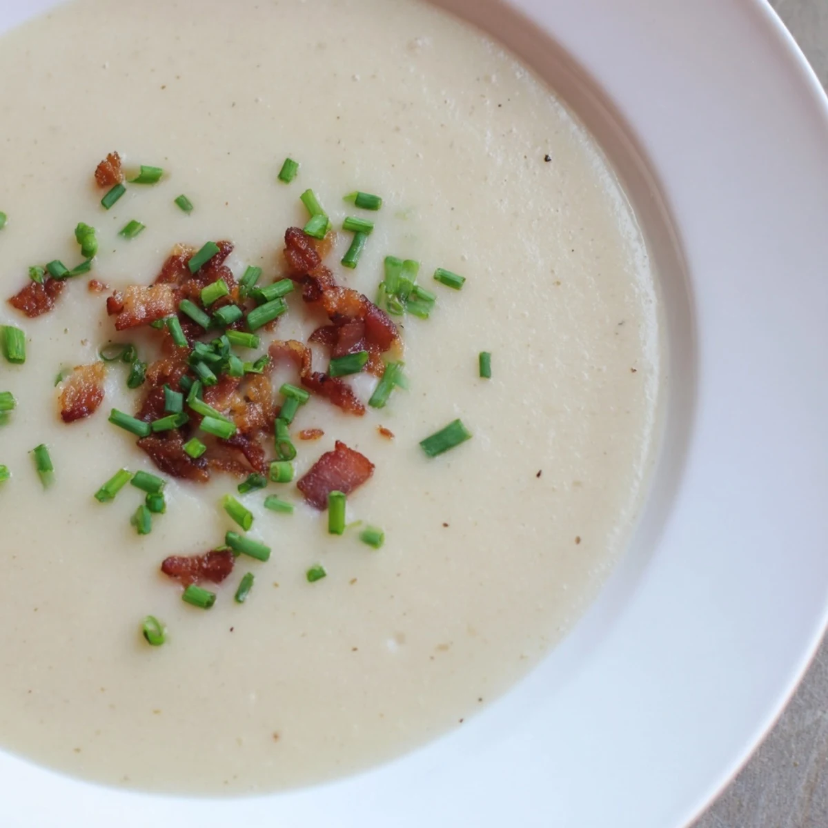 Velvety Creamy Potato and Leek Soup with Turkey Bacon in a white ceramic bowl, topped with crispy bacon pieces and vibrant green chives against a dark backdrop.