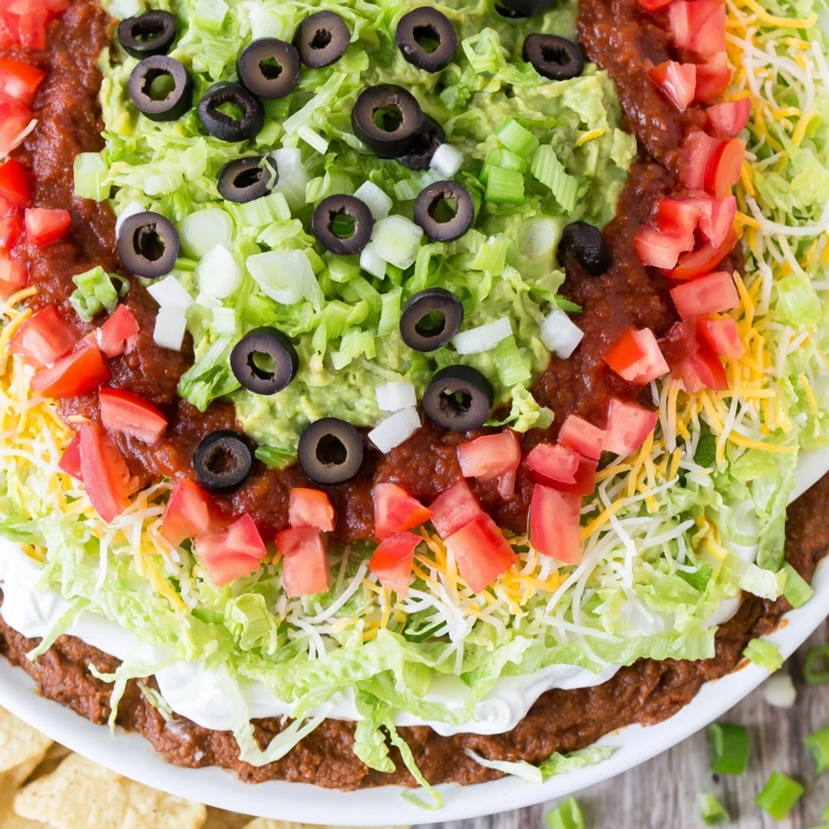 Brightly colored Ultimate Seven Layer Taco Dip with crisp tortilla chips, featuring vibrant guacamole and melted cheese.