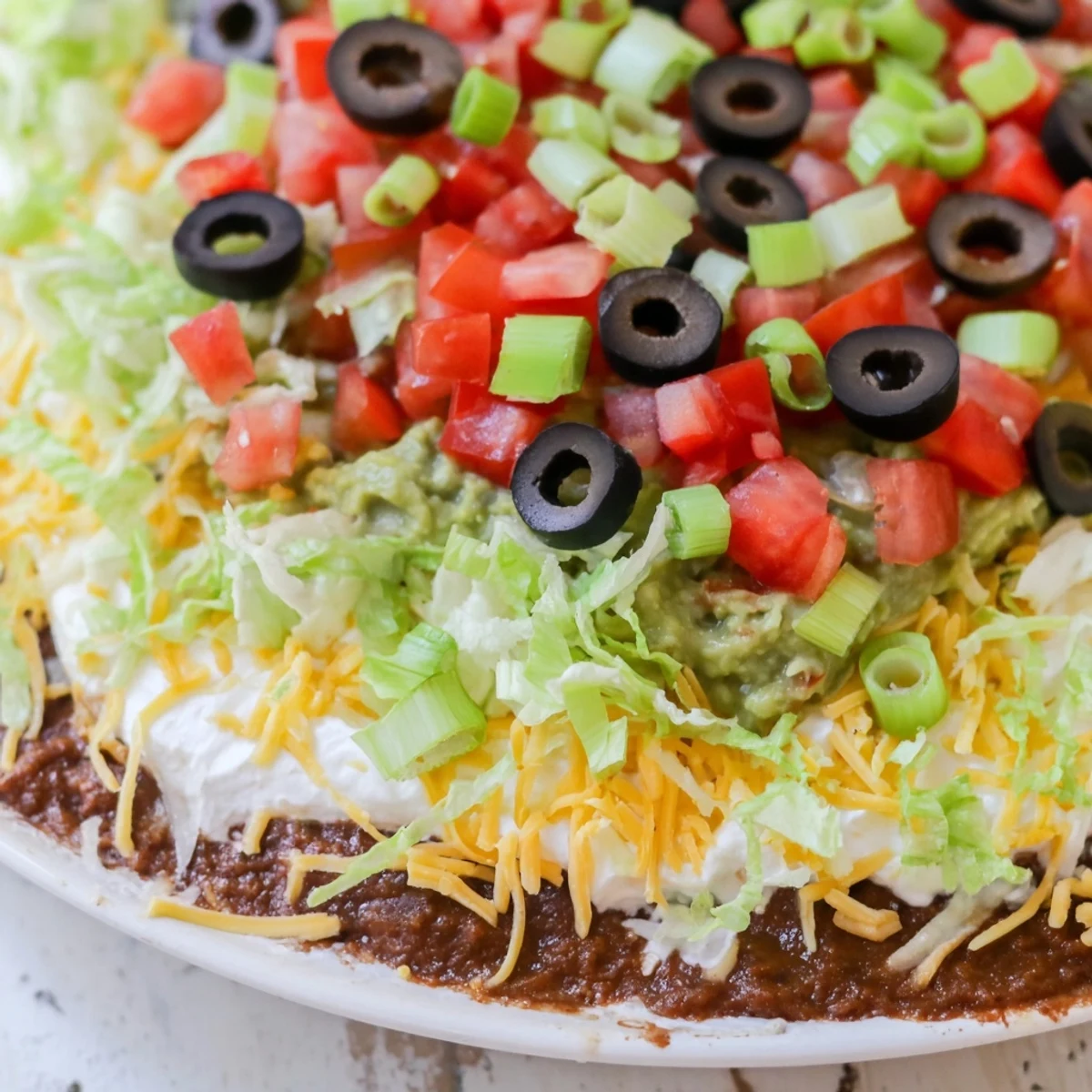 A chilled Ultimate Seven Layer Taco Dip perfect for parties, topped with shredded lettuce and ripe tomatoes.