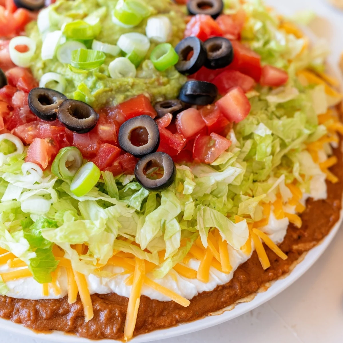 Creamy Ultimate Seven Layer Taco Dip in a glass dish, served with crunchy tortilla chips for dipping.