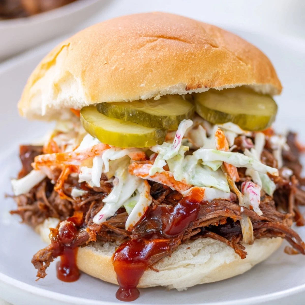 Piled high with saucy shredded brisket, crunchy cabbage slaw, and crunchy pickles, these sliders are stacked on a platter ready to serve guests.