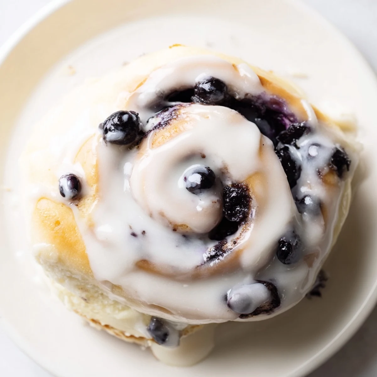 A close-up of golden Lemon Blueberry Sweet Rolls drizzled with vanilla icing, showcasing juicy blueberries and lemon zest in the swirls.  
