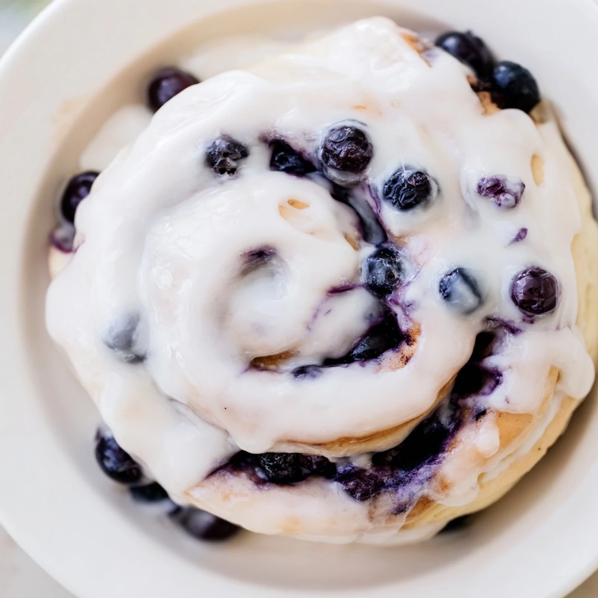 Freshly baked Lemon Blueberry Sweet Rolls on a white plate, with a drizzle of vanilla icing and scattered blueberries nearby.  