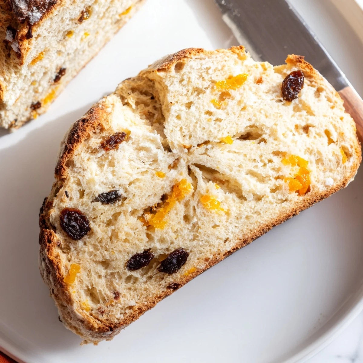 A sliced loaf of Irish Soda Bread with Raisins and Orange Zest, served with a pat of butter and orange marmalade on a plate.  