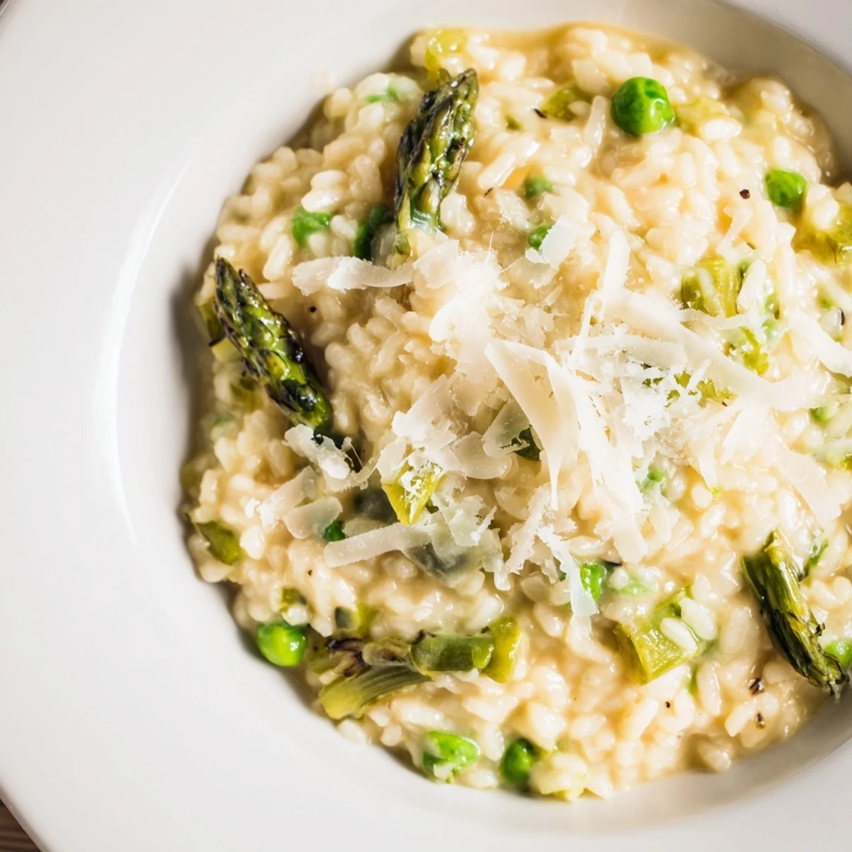 Spring-inspired Asparagus and Pea Risotto with Parmesan garnished with extra cheese, served on a rustic wooden table for dinner.