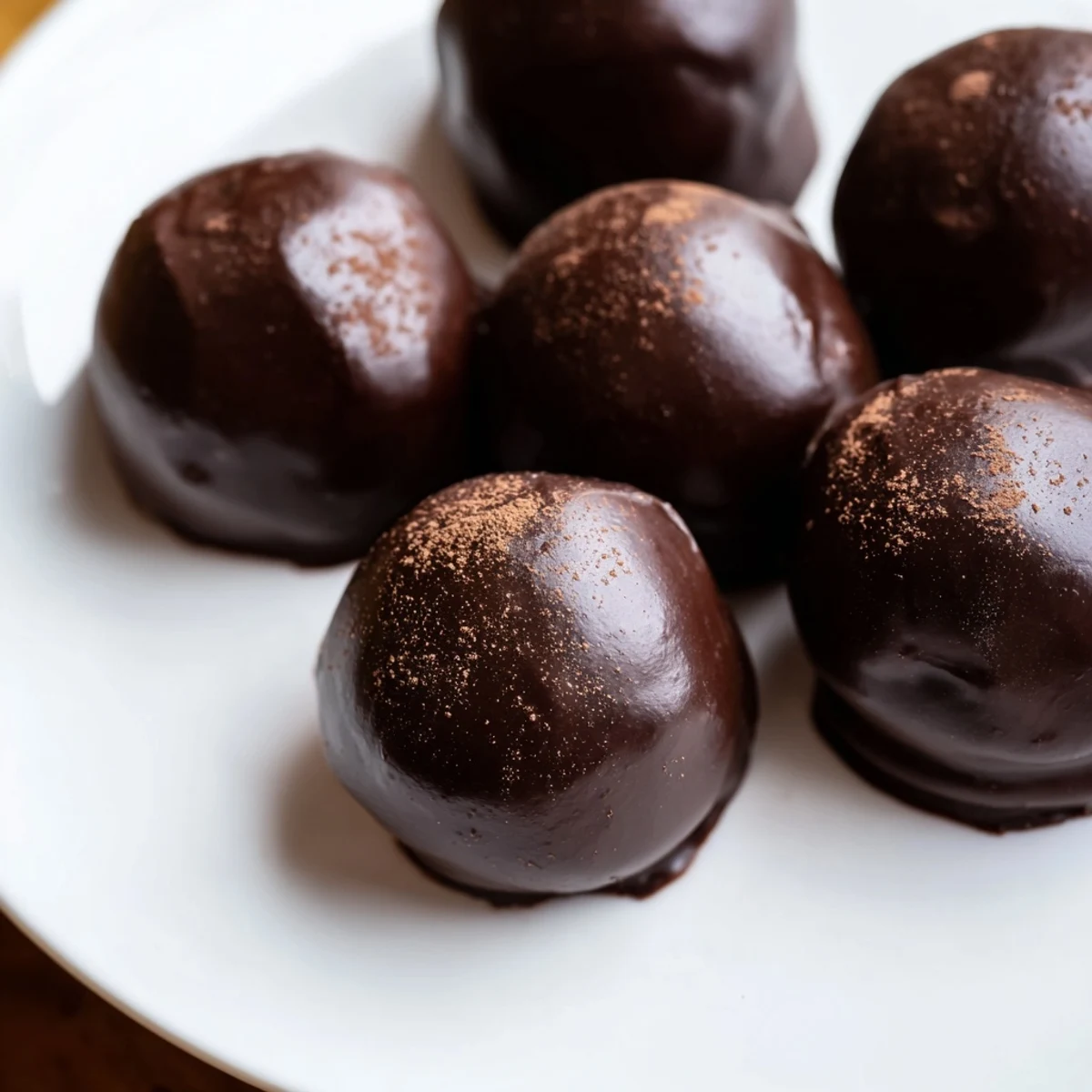 A close-up of Irish Cream Truffles with Dark Chocolate glistening on a plate, dusted with cocoa powder.  