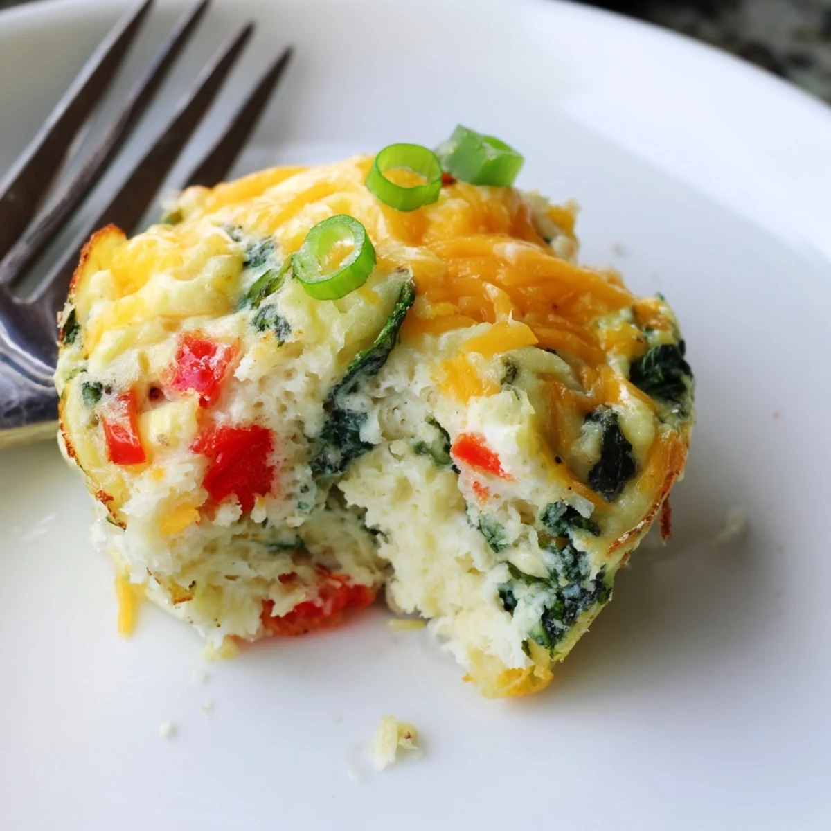 A close-up of fluffy cottage cheese egg bites reveals a soft, creamy texture, topped with melted cheddar and a sprinkle of savory smoked paprika.