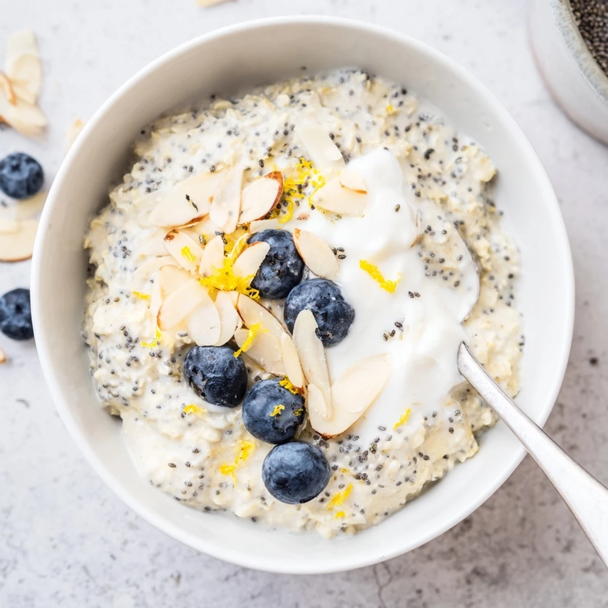 A spoon stirs the tangy, plant-based breakfast, with lemon zest and poppy seeds visible against the oats.