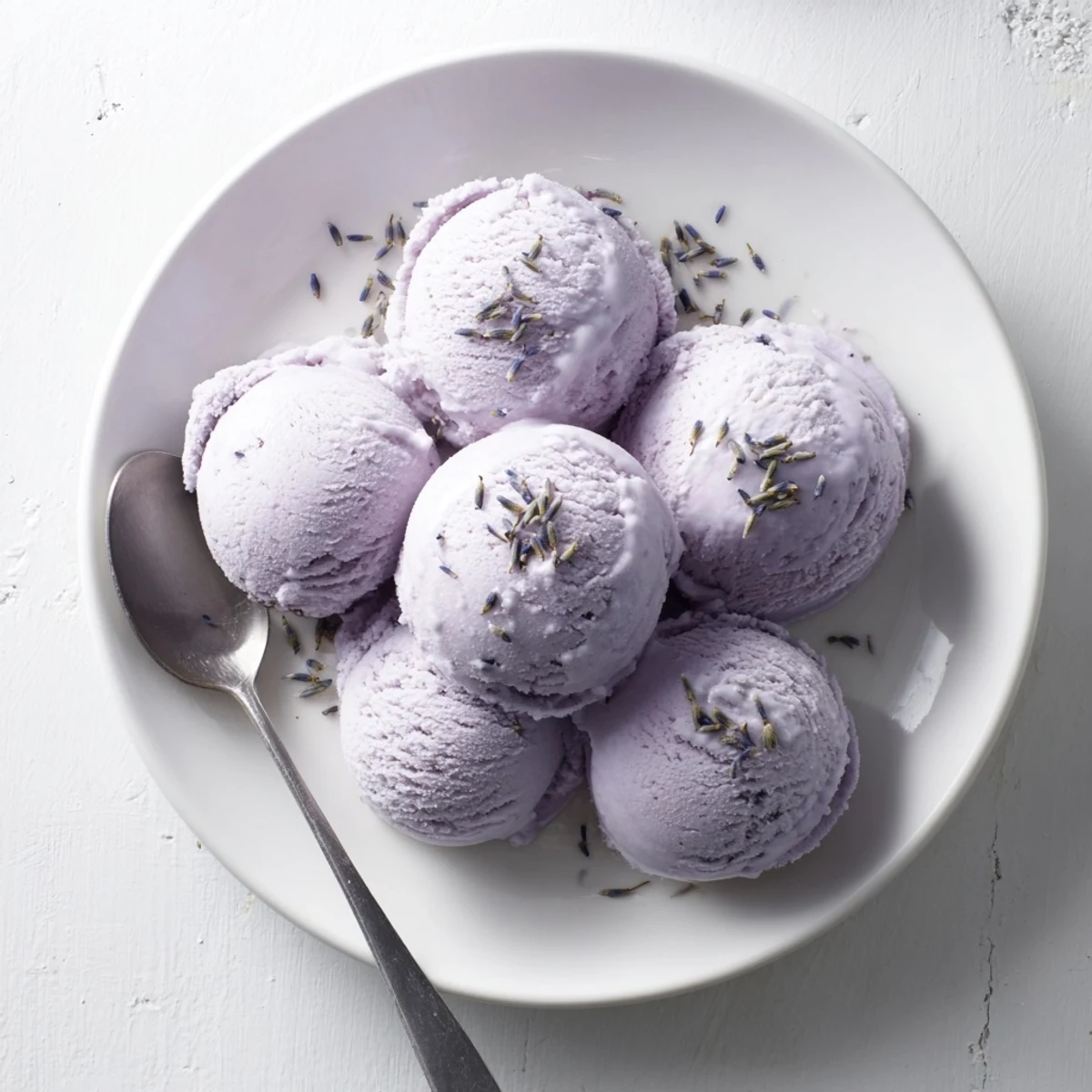 A single scoop of lavender ice cream in a clear glass bowl garnished with dried lavender buds.