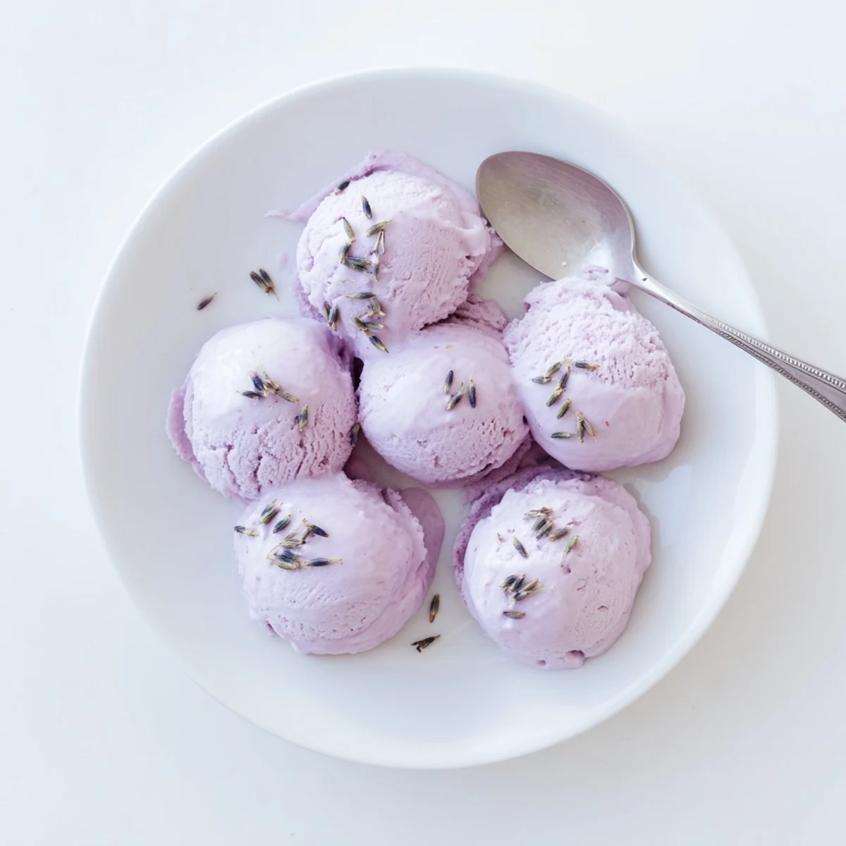 Lavender ice cream served in a vintage glass dish on a marble counter beside fresh blueberries.