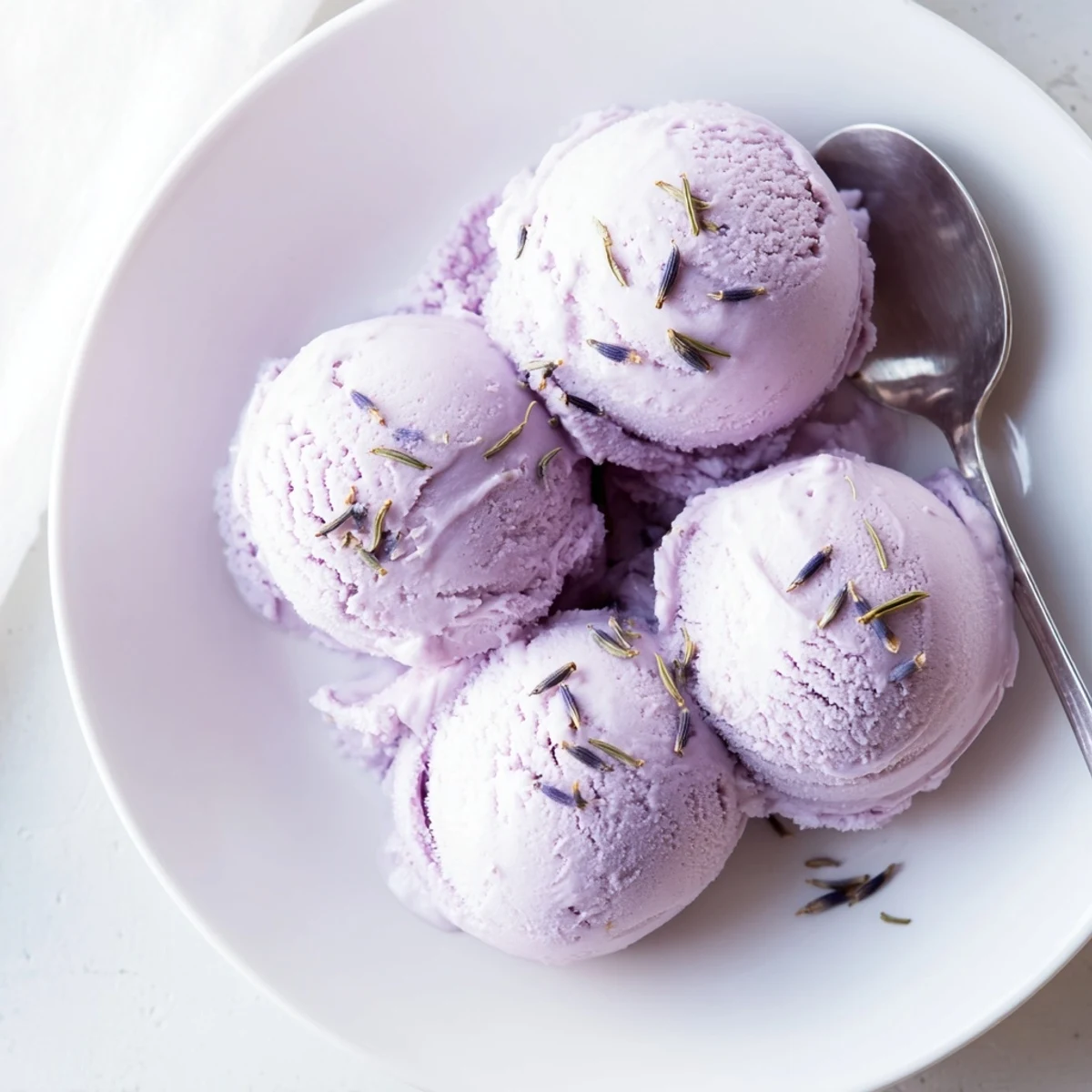 A close-up of creamy lavender ice cream in a waffle cone with edible flower petals.