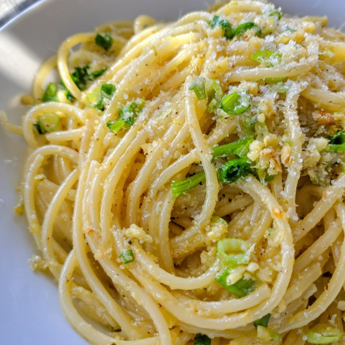 Steamy, golden noodles glisten in a skillet for this Garlic Noodles recipe, topped with fresh scallions and sesame seeds.