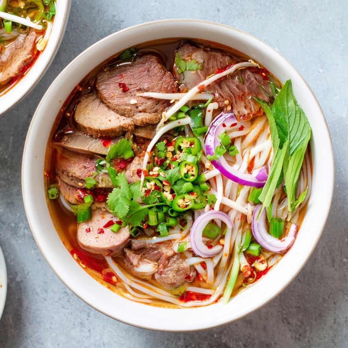 Steaming bowl of Bun Bo Hue with thick rice noodles, tender beef slices, and fresh herbs.