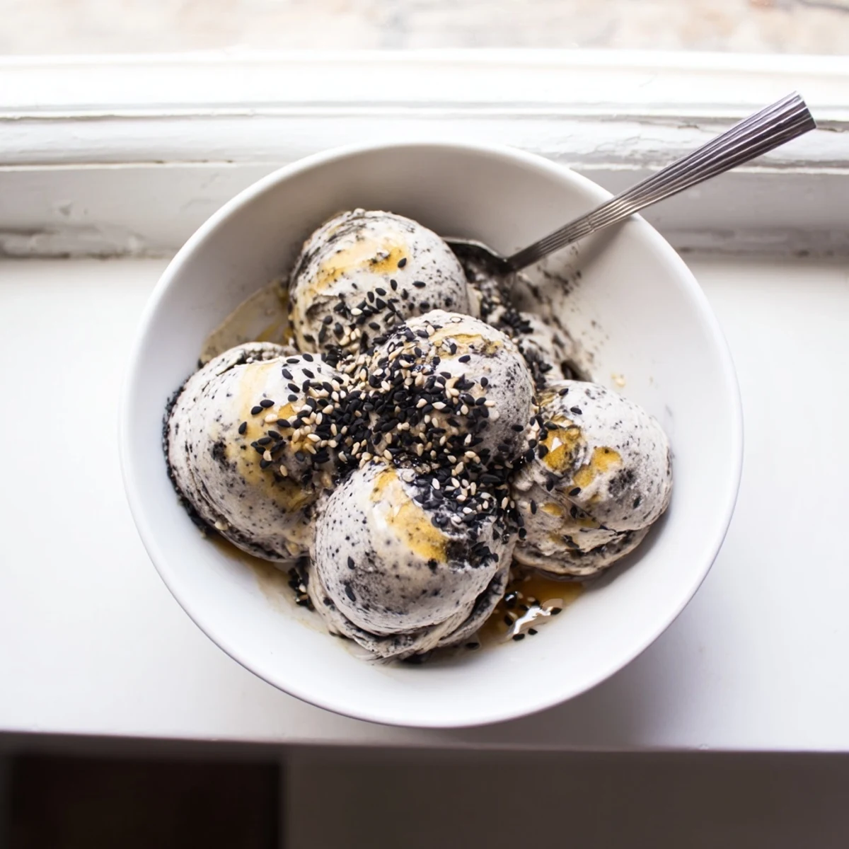 Freshly churned Toasted Black Sesame Ice Cream served in a waffle cone, with visible black sesame specks throughout.