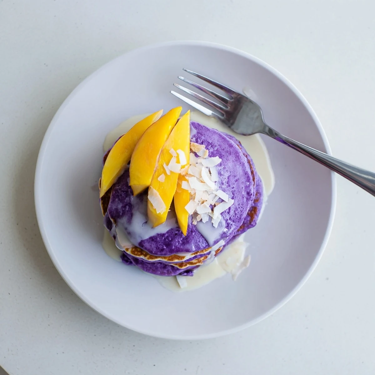 Vibrant purple ube mochi pancakes stacked high, fresh off the griddle and ready for sweet toppings.