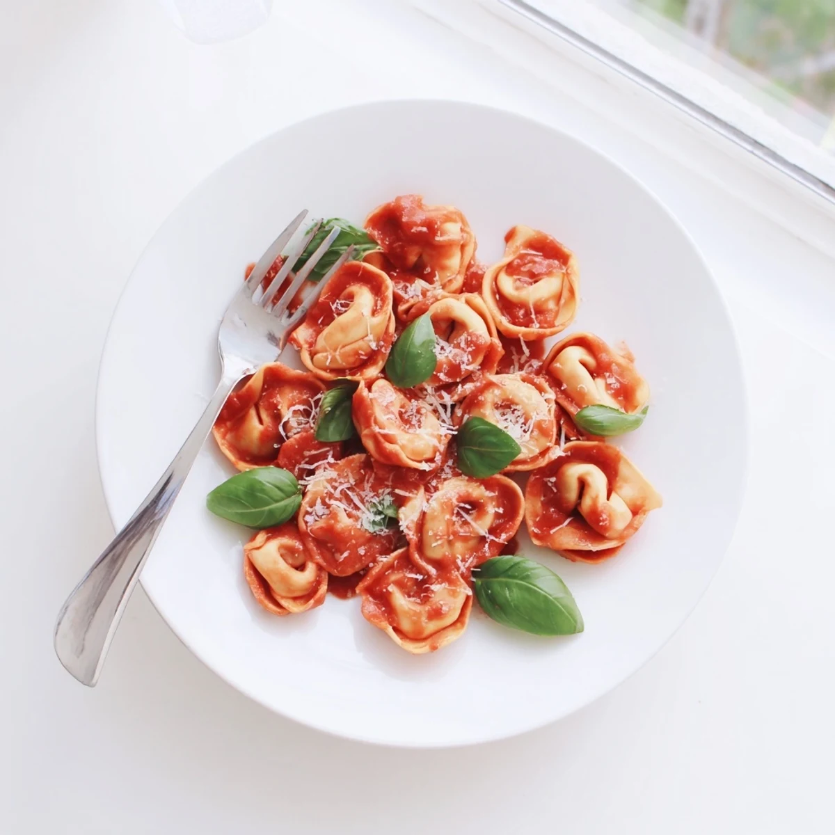 Close-up of tender Mozzarella Tortellini tossed in light tomato sauce, topped with fresh basil leaves and Parmesan cheese.