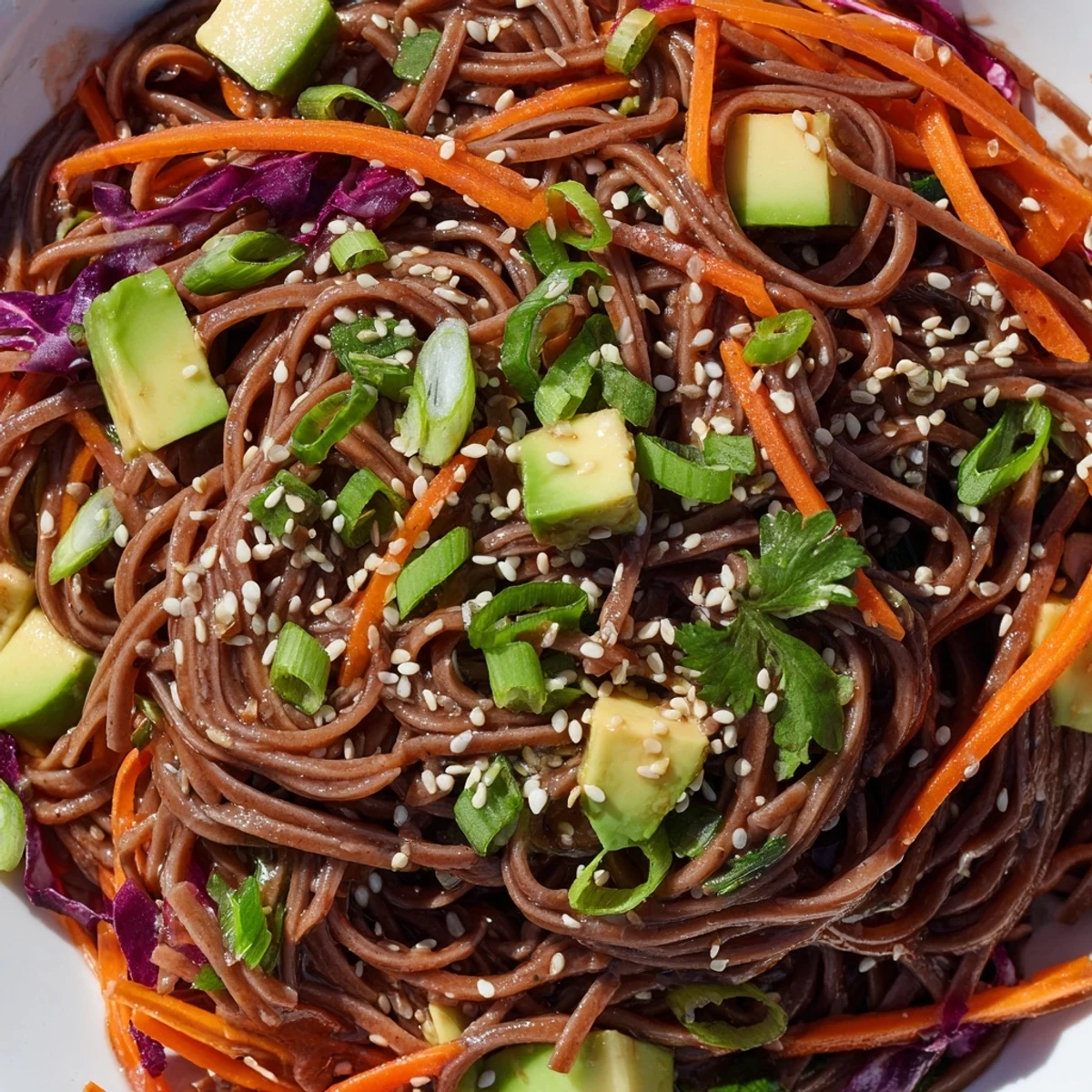 Close-up view of Sesame Avocado and Soba Noodle Salad highlighting creamy avocado chunks tossed with crisp cucumber and fresh green onions.