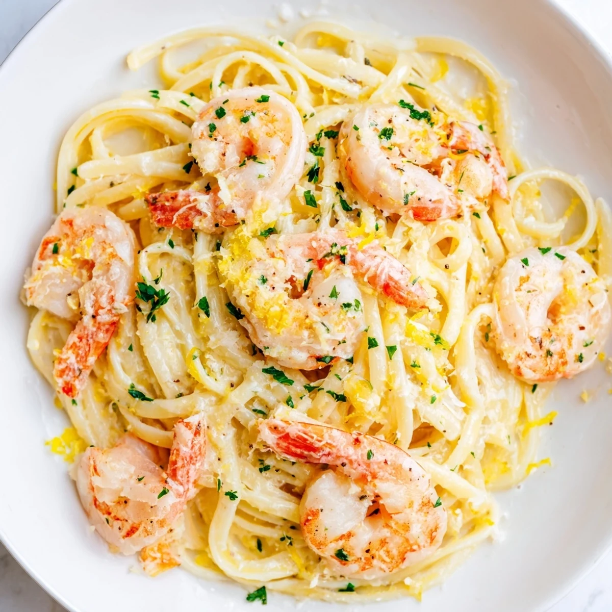 Close-up of shrimp scampi garlic cream pasta garnished with lemon wedges and grated parmesan on white plate