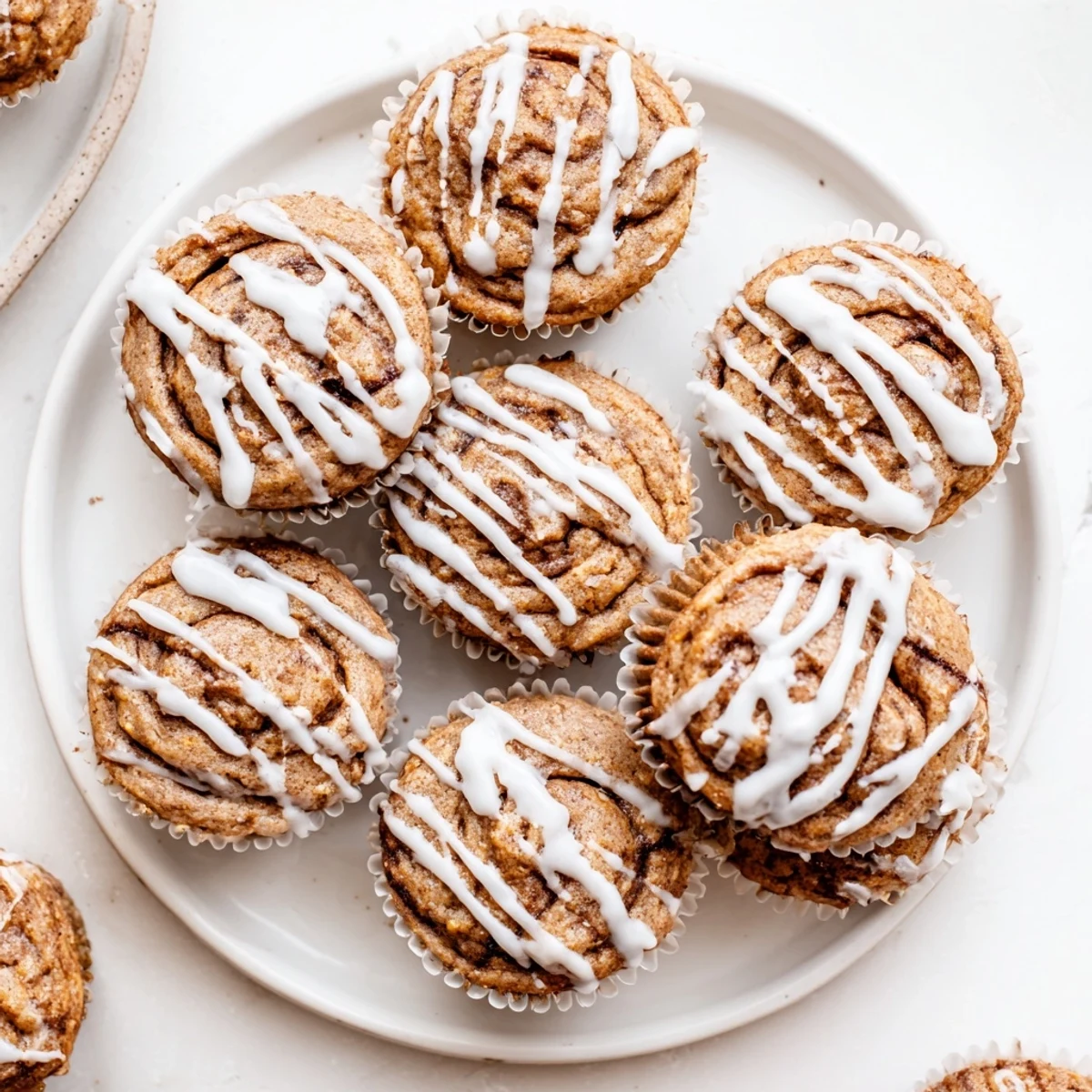 Freshly baked cinnamon roll protein muffins with golden swirls and creamy white icing drizzle