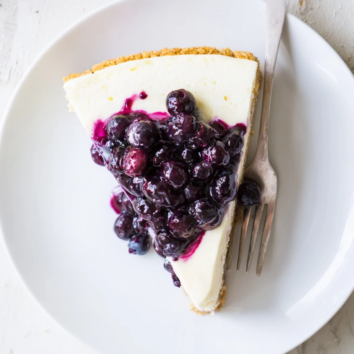 Creamy blueberry cheesecake slice with glossy purple topping on graham cracker crust