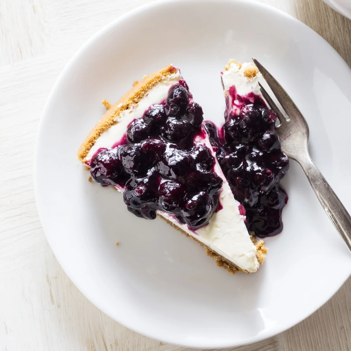 Velvety blueberry cheesecake topped with glossy blueberry sauce on a buttery graham cracker crust