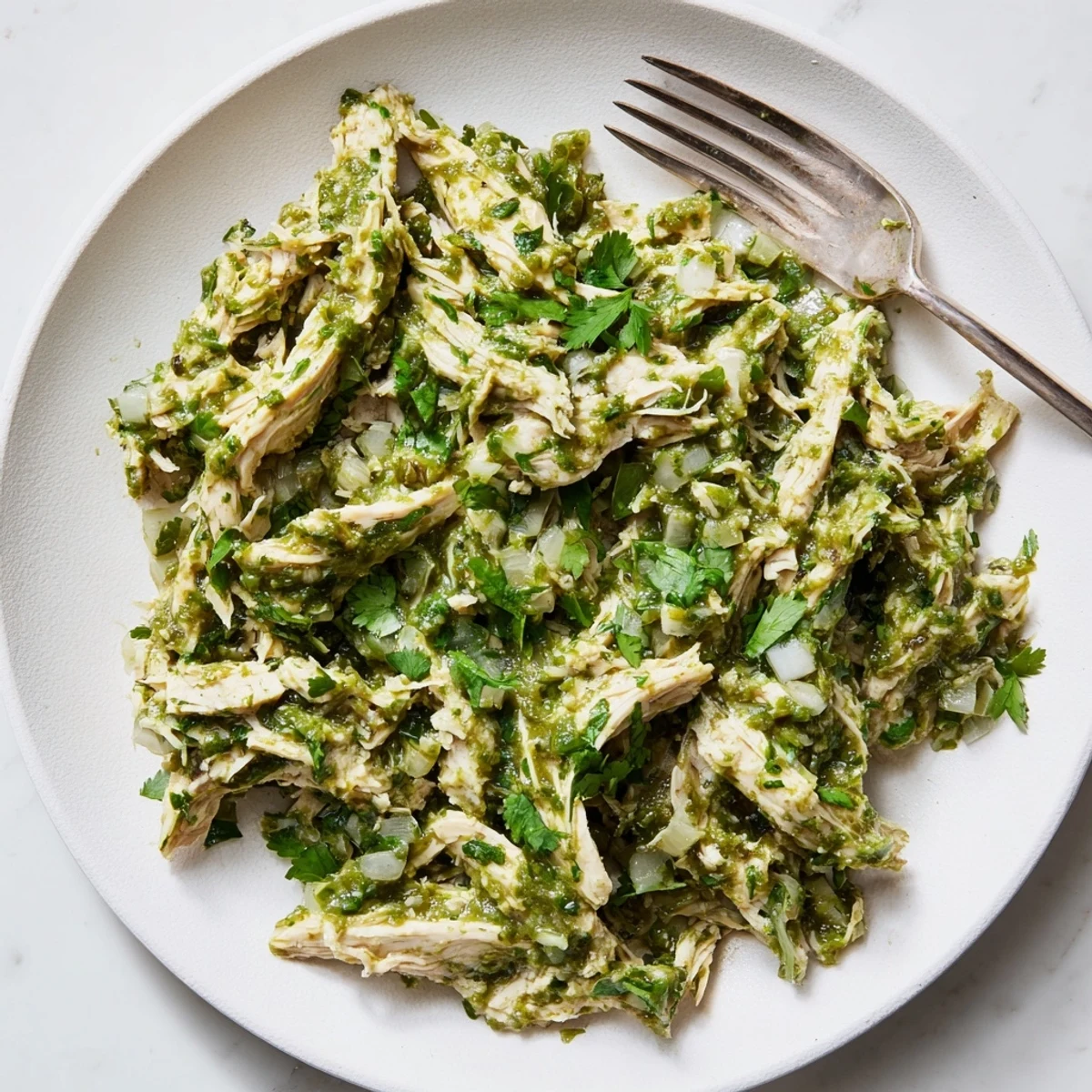 Golden shredded chicken breasts swimming in vibrant green salsa verde sauce, topped with fresh cilantro for Taco Tuesdays