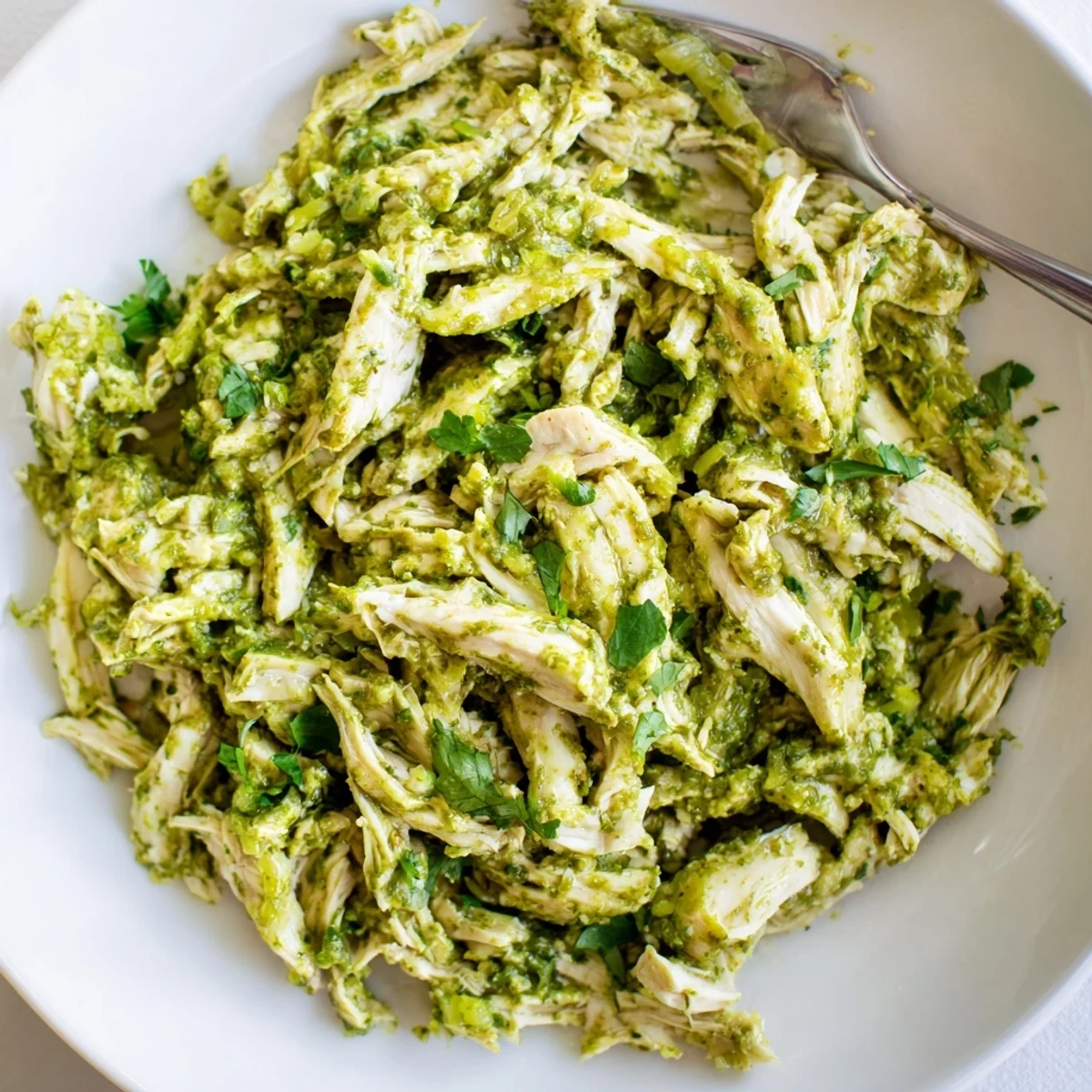 Savory salsa verde chicken shredded and plated with avocado slices, red onion, and lime wedges for a festive Mexican dinner
