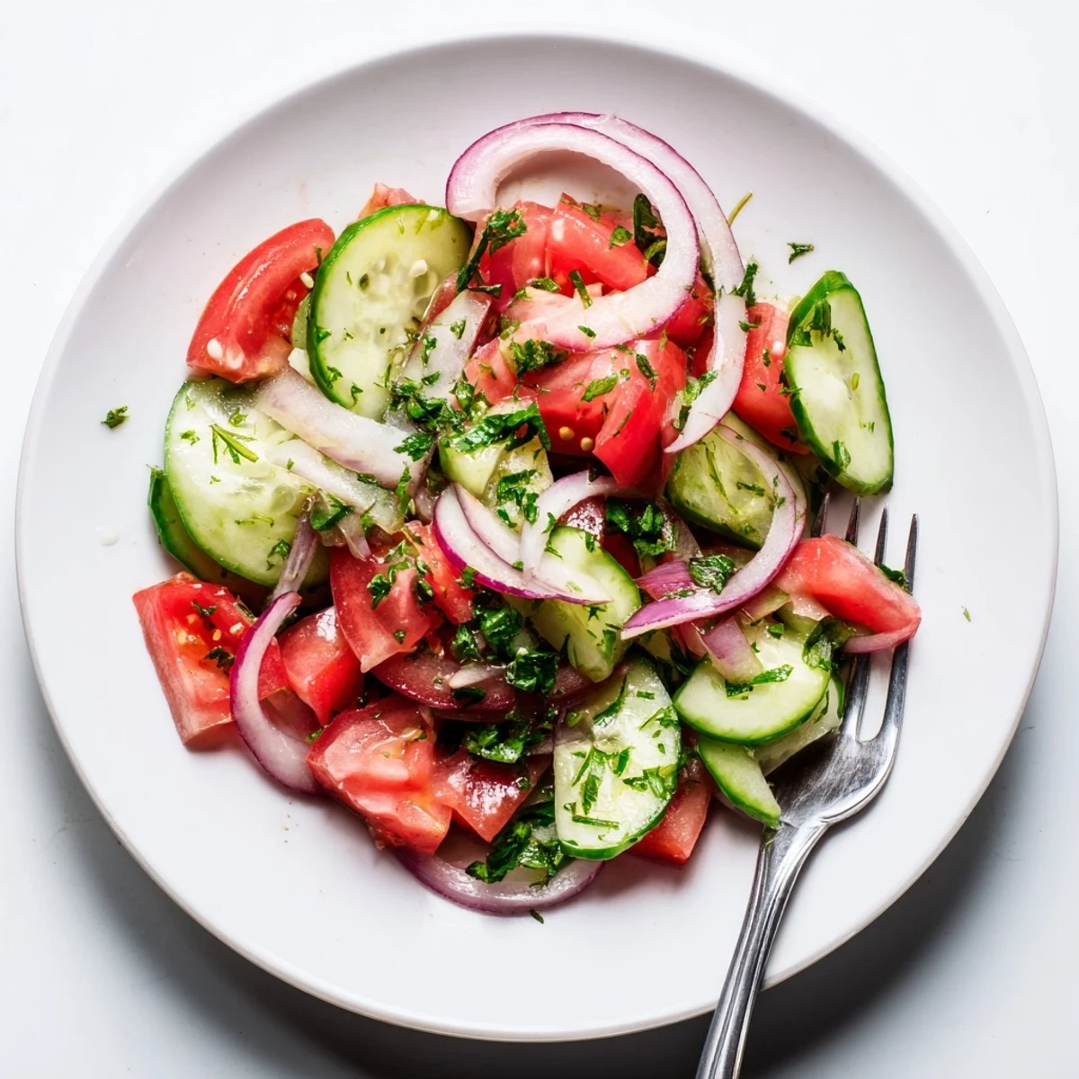 Summer tomato, cucumber, and onion salad drizzled with olive oil dressing and fresh herbs