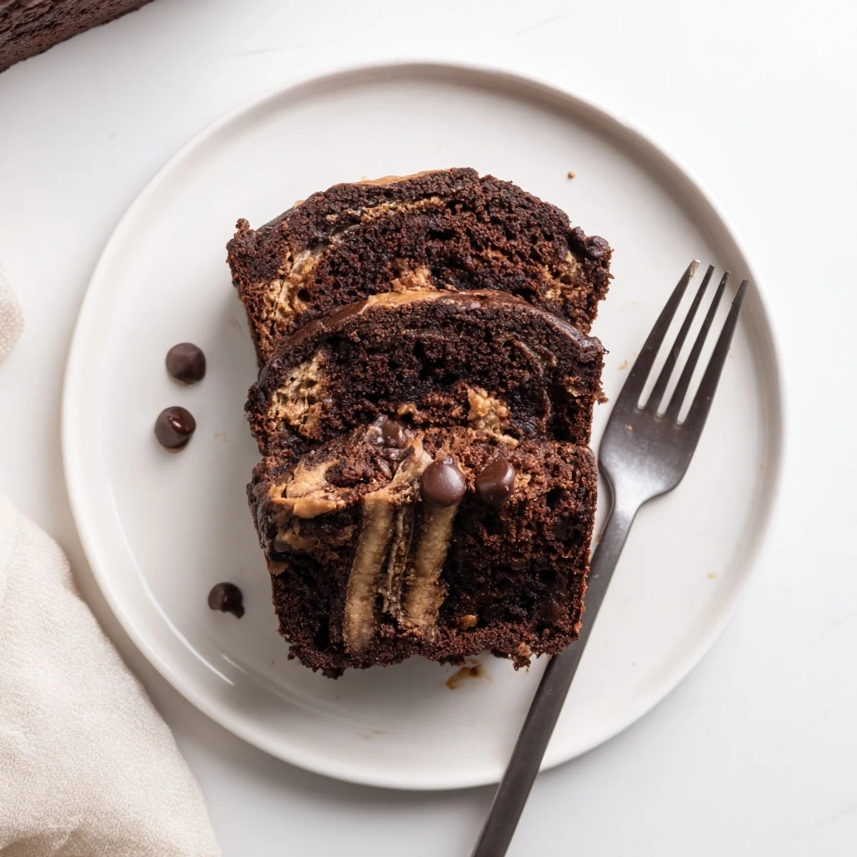 Thick slice of chocolate peanut butter banana bread topped with creamy peanut butter drizzle and chocolate chips