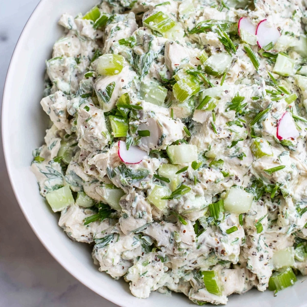 Creamy green goddess chicken salad dip topped with fresh herbs and sliced vegetables