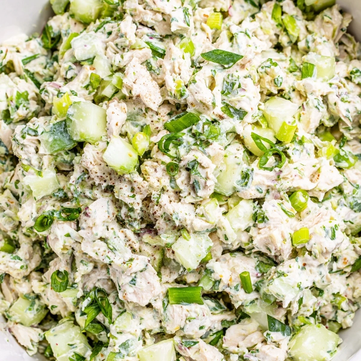 Golden chicken pieces mixed in vibrant green herb dressing served in white bowl