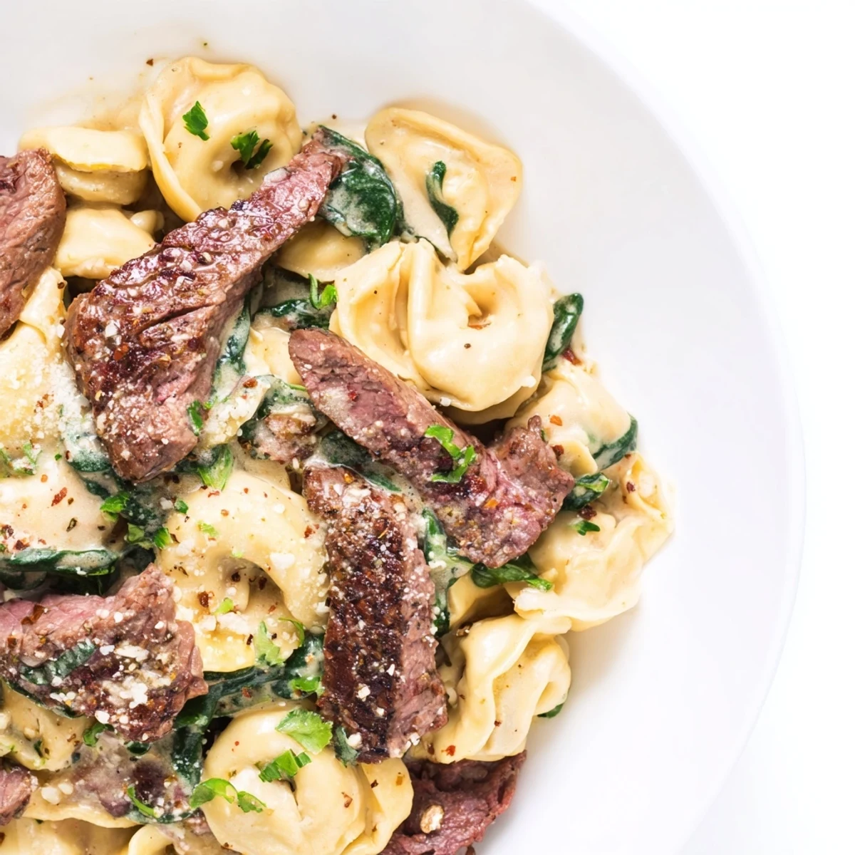 Golden garlic steak tortellini in creamy white sauce topped with fresh parsley and Parmesan