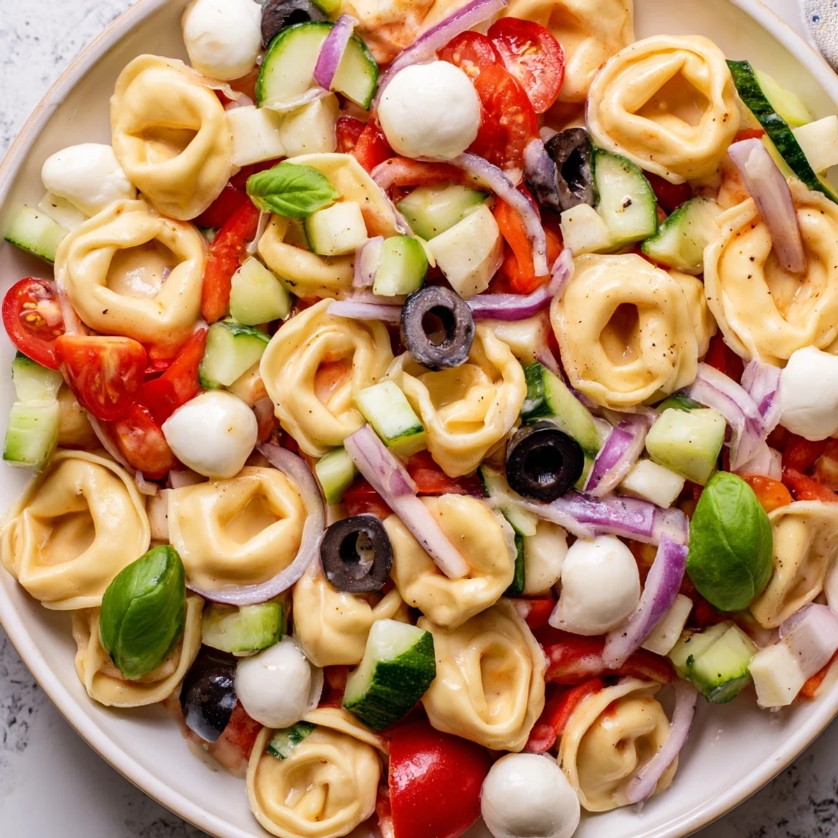 Cheese tortellini salad glistening with herb dressing, crisp vegetables, and fresh basil leaves