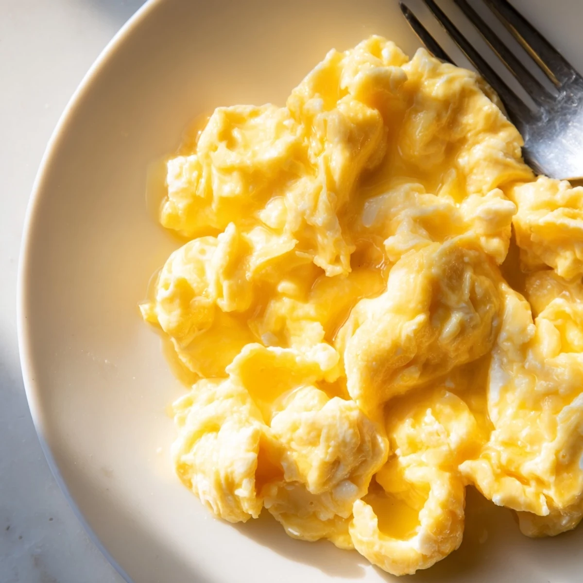 Creamy scrambled eggs piled on a plate with golden buttery curds glistening warmly