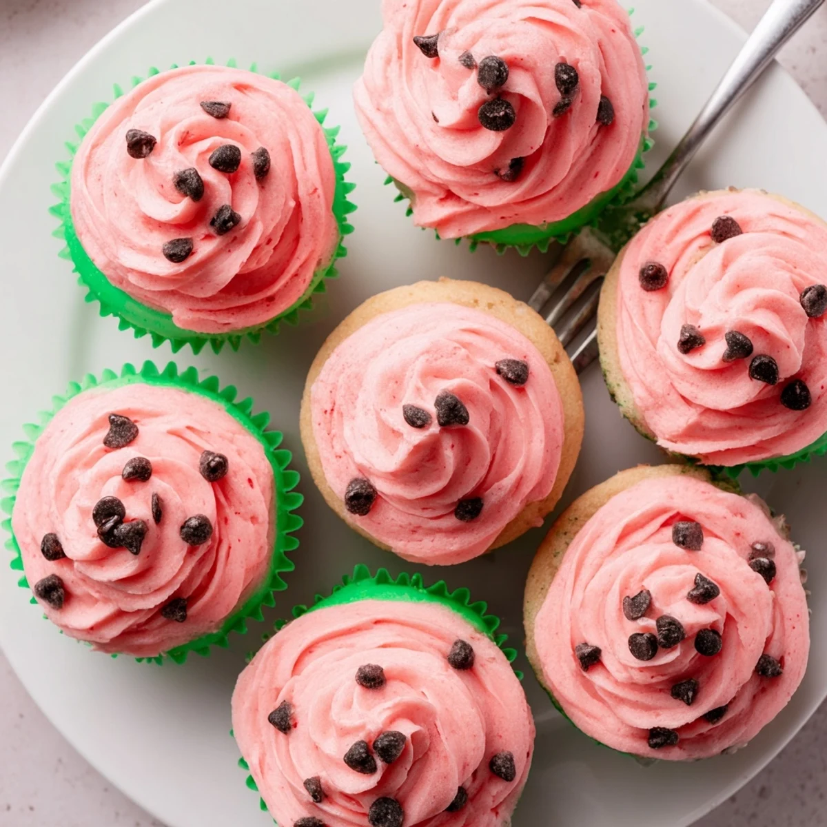 Freshly baked watermelon cupcakes topped with creamy pink frosting and black seed sprinkles on serving tray