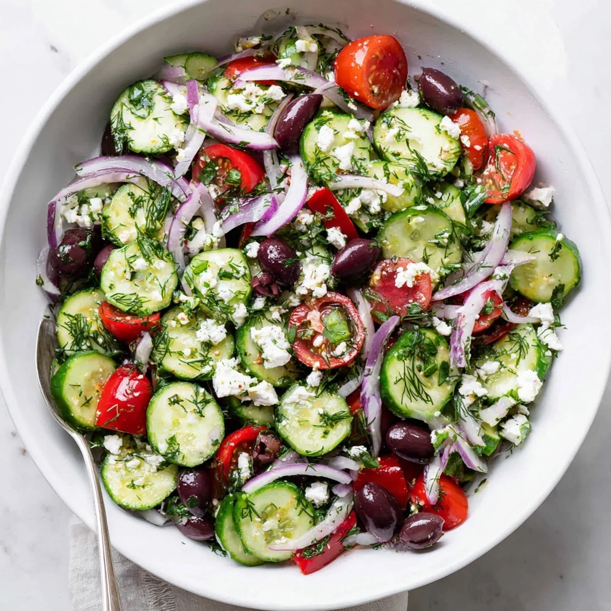 Colorful bowl of Mediterranean cucumber salad featuring juicy tomatoes, olives, and crumbled feta tossed in lemon herb dressing