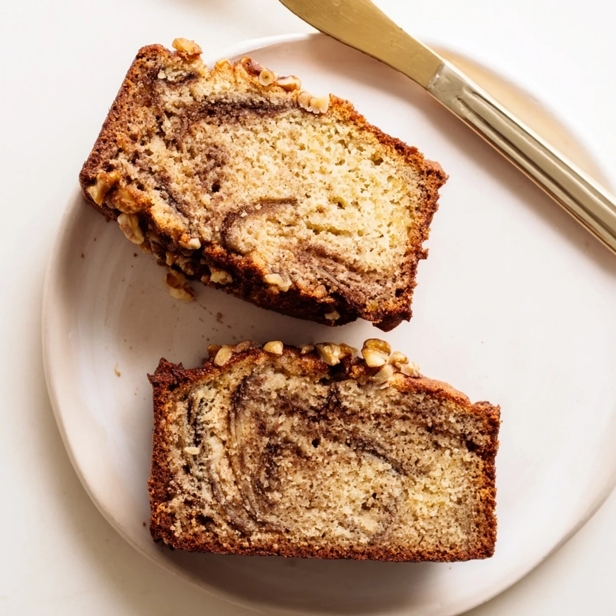 Moist banana bread slice revealing marble cinnamon swirl layers topped with crunchy walnuts on a white plate