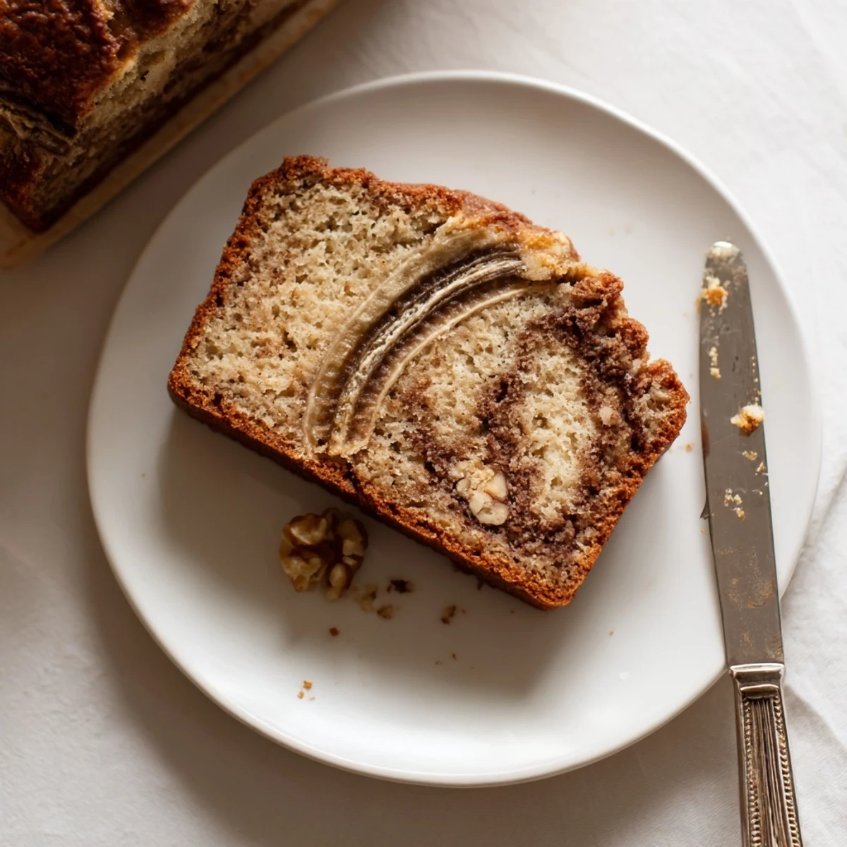 Golden brown banana nut bread loaf with cinnamon swirl and chopped walnuts on a wooden cutting board