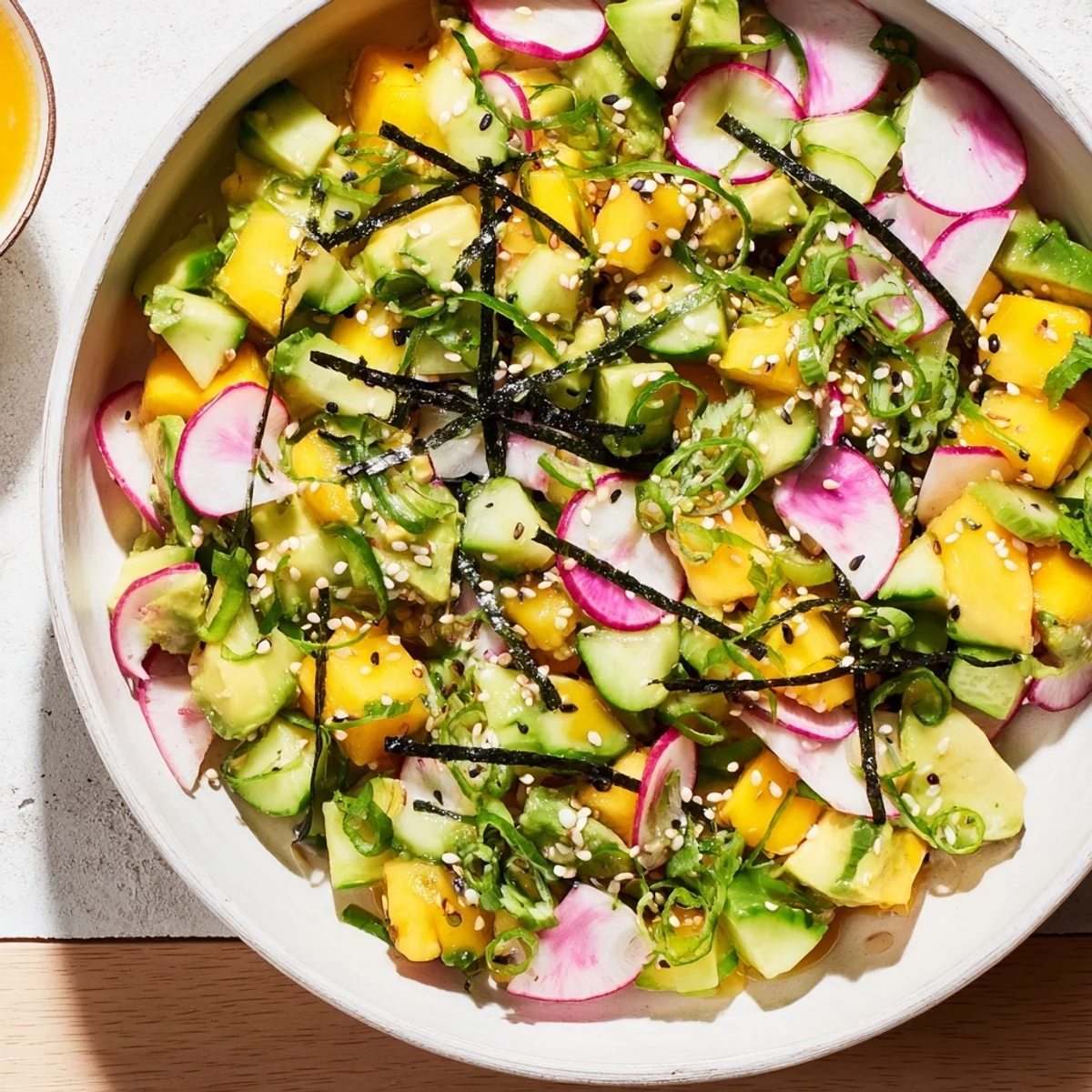 Refreshing avocado mango poke salad arranged with cucumber radishes and scallions topped with nori strips