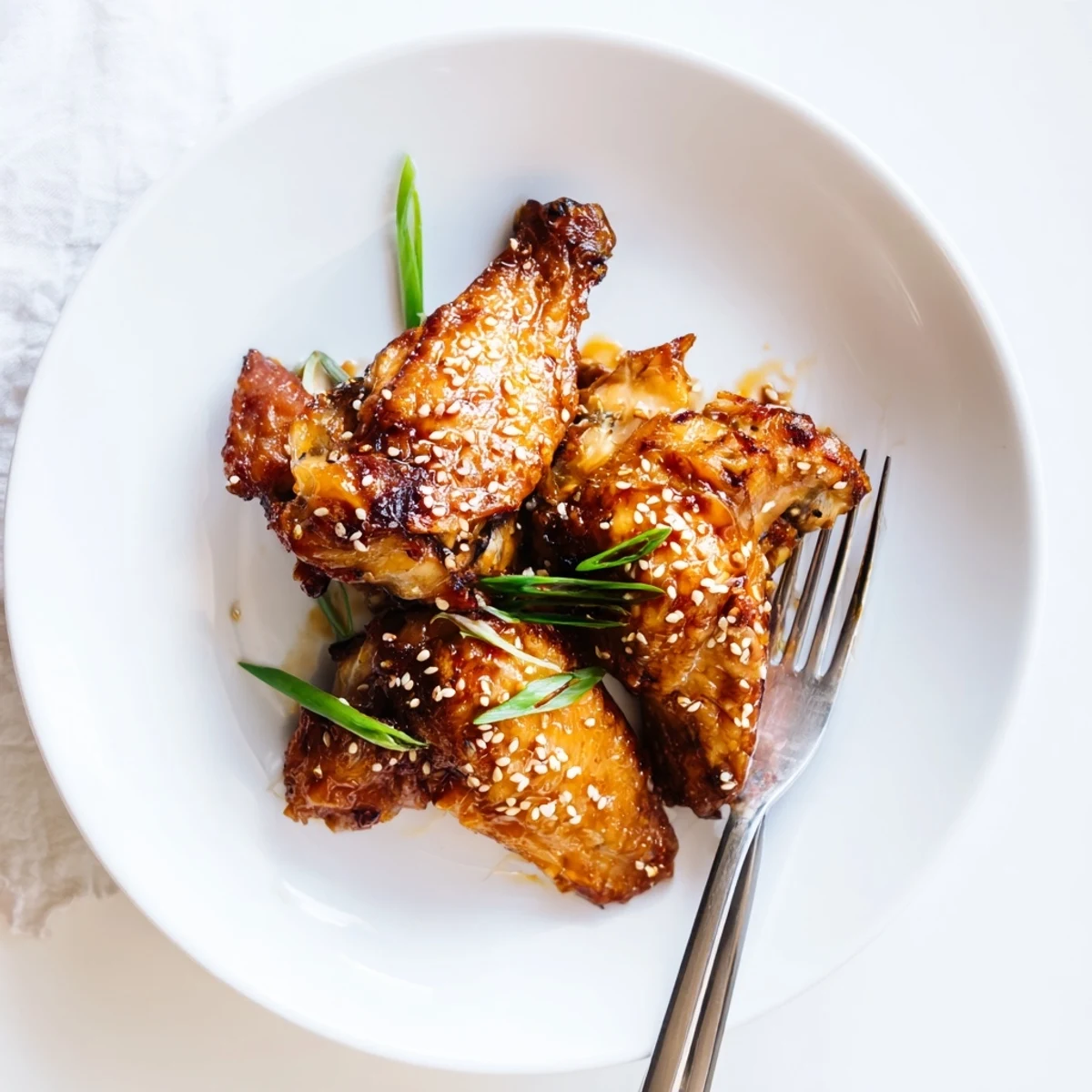 Sticky miso honey marinated chicken wings piled on a platter sprinkled with sesame seeds and scallions