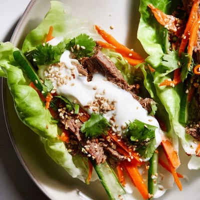 Rolled lettuce leaves filled with tender beef, shredded carrots, and cucumbers are plated for a low-carb Beef Wrap with Lettuce.