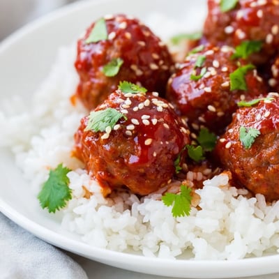Tender Spicy Sriracha Beef Meatballs glazed in a glossy red sauce, topped with sesame seeds.