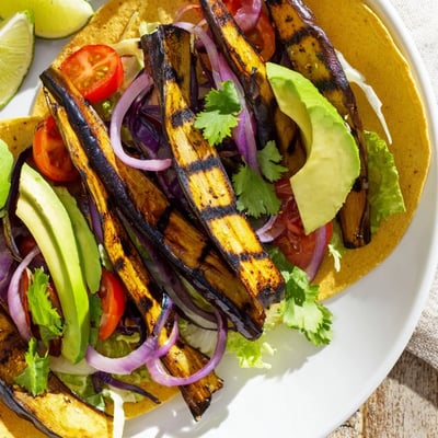 Charred Eggplant Tacos stacked with avocado slices and red onion, served with lime wedges on a rustic plate.