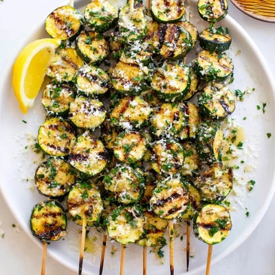 Grilled Garlic Butter Zucchini Skewers served with lemon wedges and fresh parsley on a platter.
